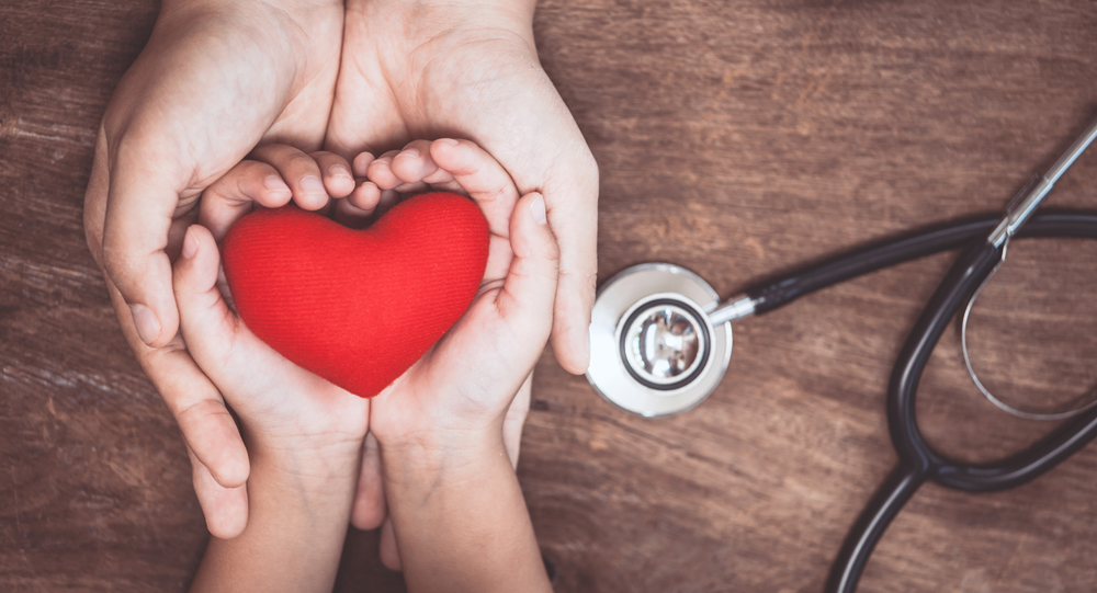 Hands holding heart next to a stethoscope